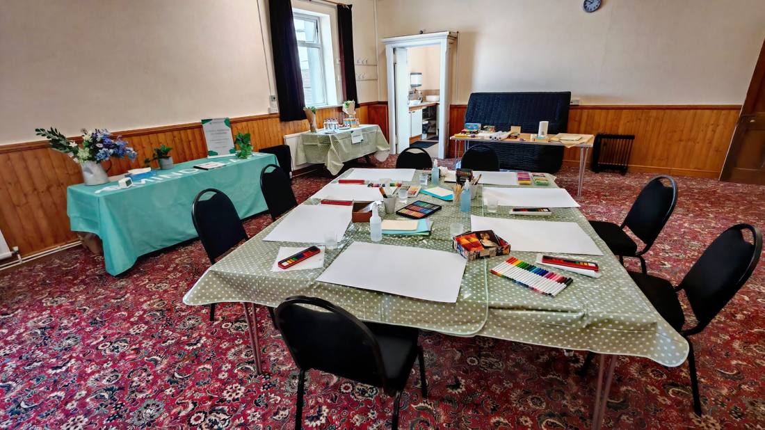 A community hall set up for an art session, with paper and pastels on the tables